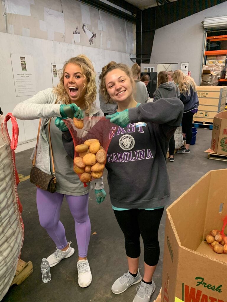 Two girls hold bag of sweet potatoes