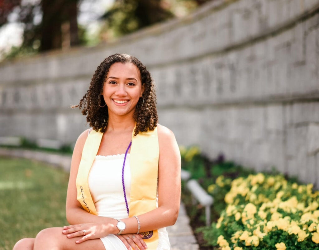 female graduate sitting on the ground in front of a gray wall