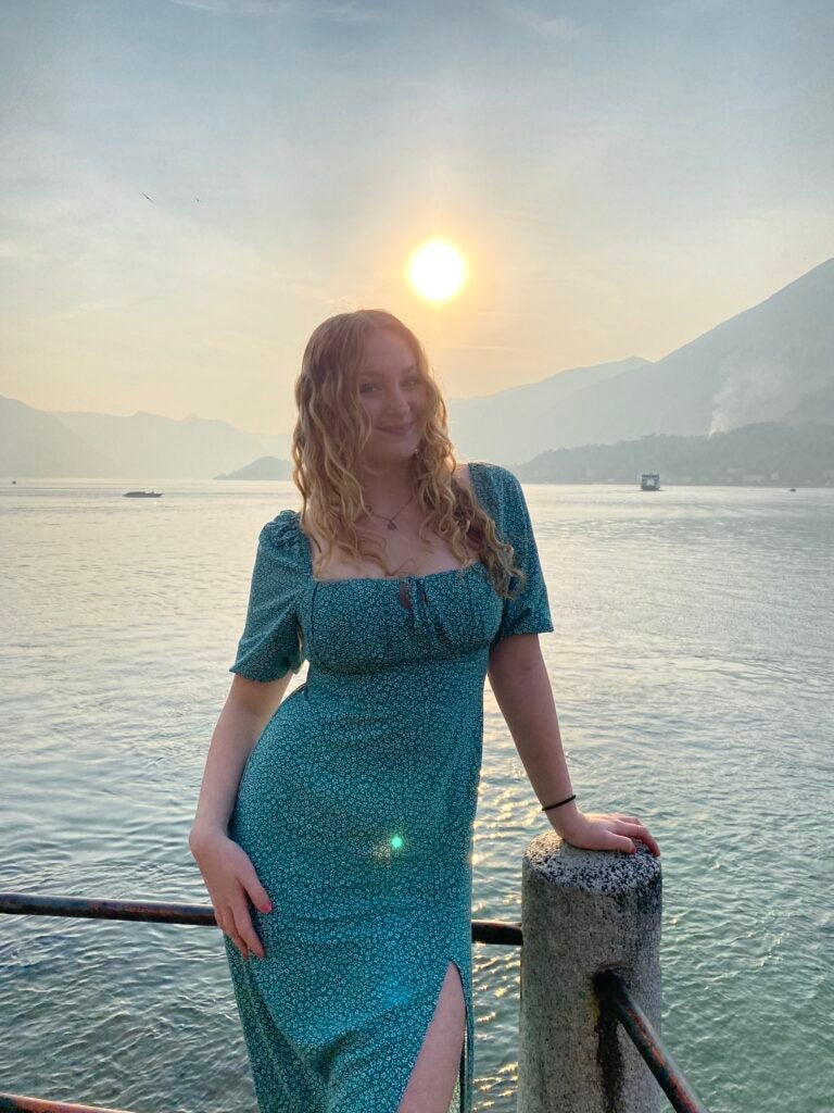 young woman in a blue dress standing on a dock in front of the water