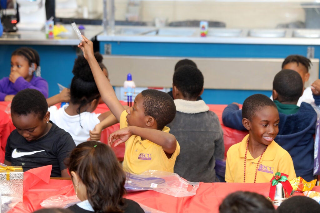 Student sitting at cafeteria table raises hand