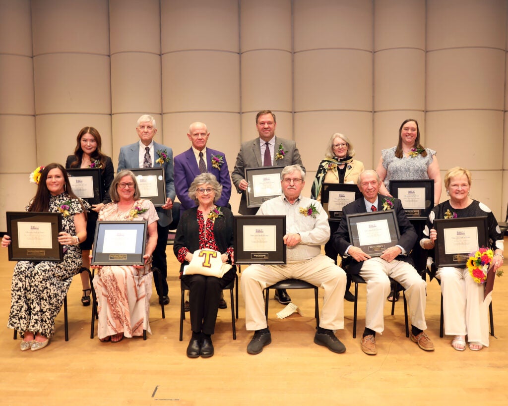 People sit on stage holding their educators hall of fame plaques