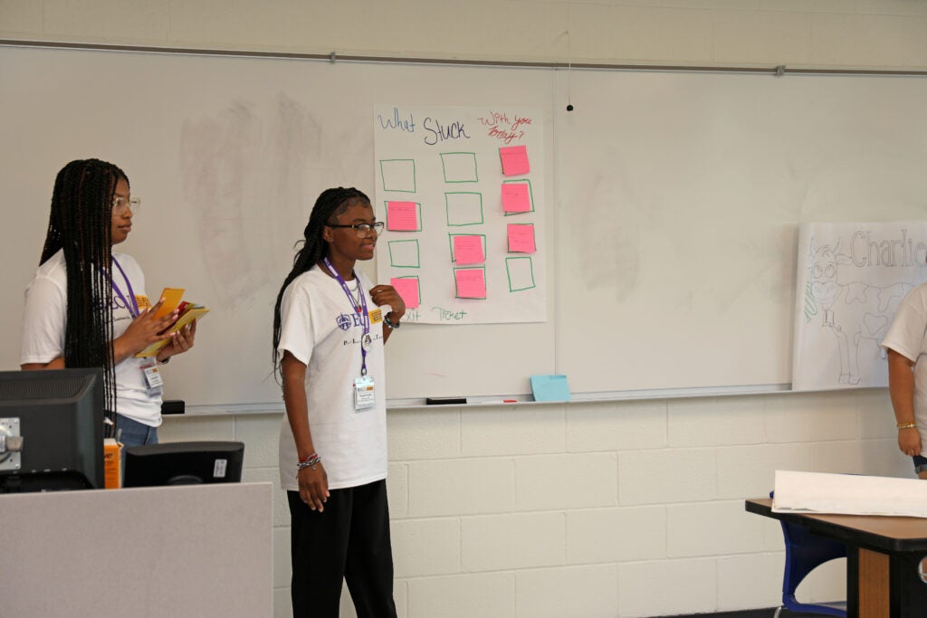 Students standing at white board pointing to sticky notes