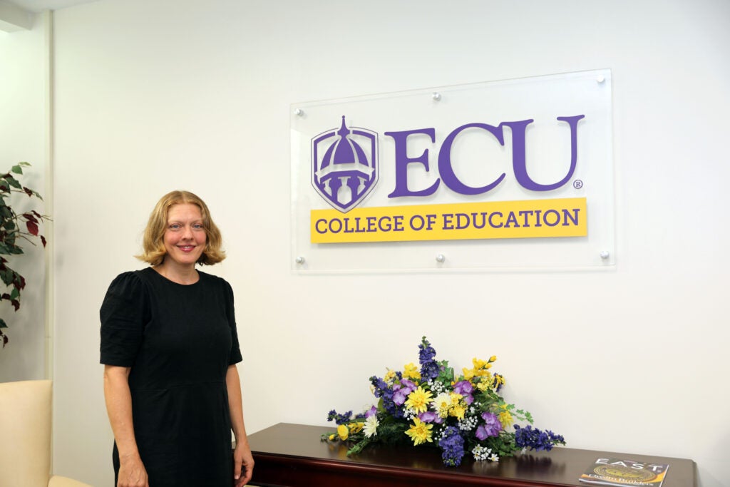 Tanya Christ standing in front of COE sign in dean's suite