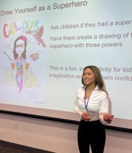 Sarah Wall presents in front of board with instructions on drawing yourself as a superhero