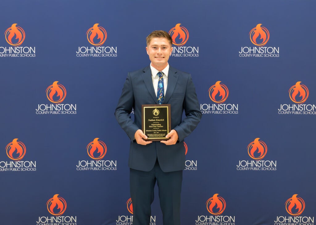 man stands in front of a blue backdrop holding an award