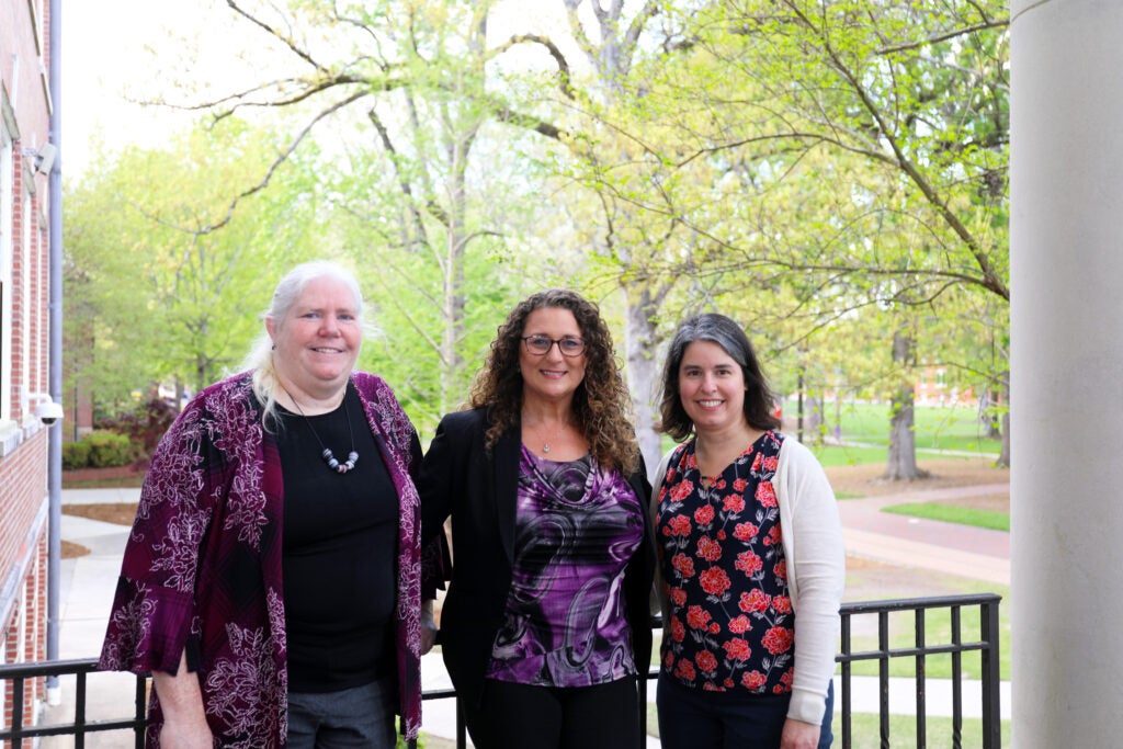 Three women pose for a photo in front of a railing