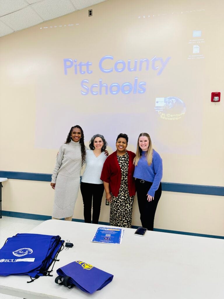 four counselor education faculty posing under Pitt Count Schools sign