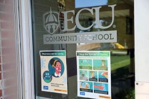 Main entrance of the ECU Community School with signs asking people to wear cloth face coverings and how to stop the spread of germs