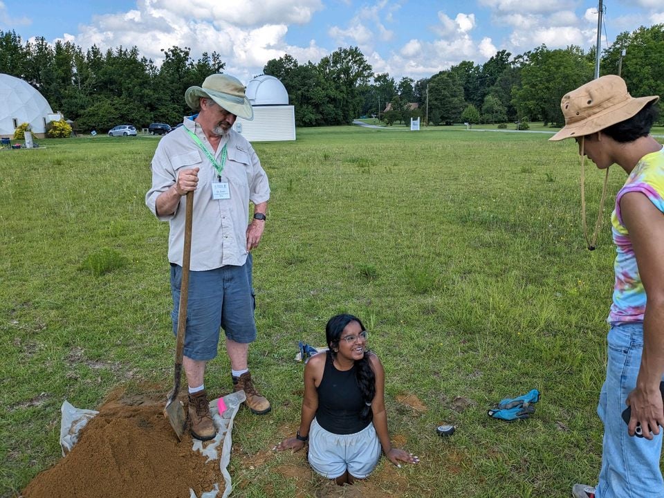 Girl standing in hole with other researchers standing around