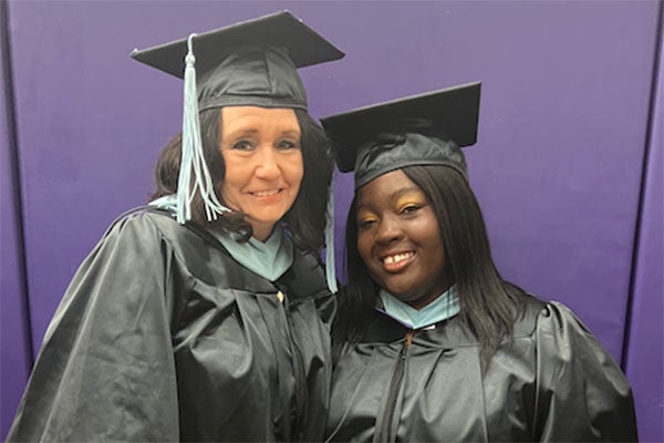 Two women in master’s caps and gowns at graduation